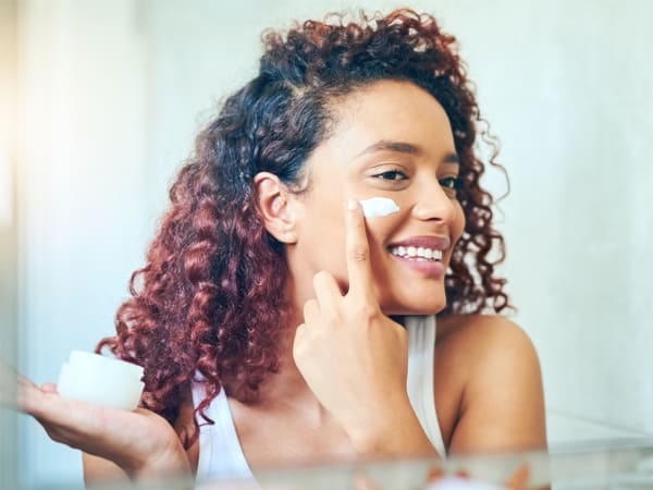 young woman using face cream in mirror